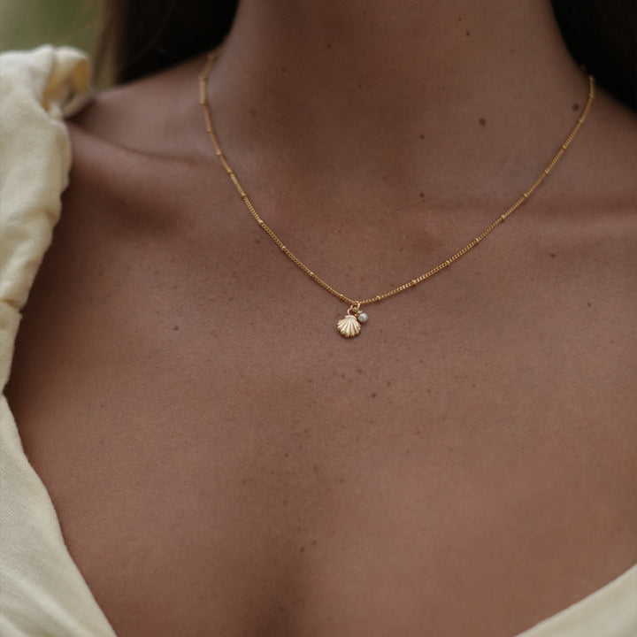 woman wearing a gold necklace with a shell charm