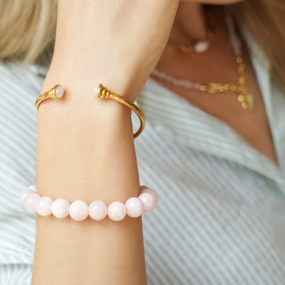 woman wearing gold bangle bracelet with graduated ends with light pink gemstones