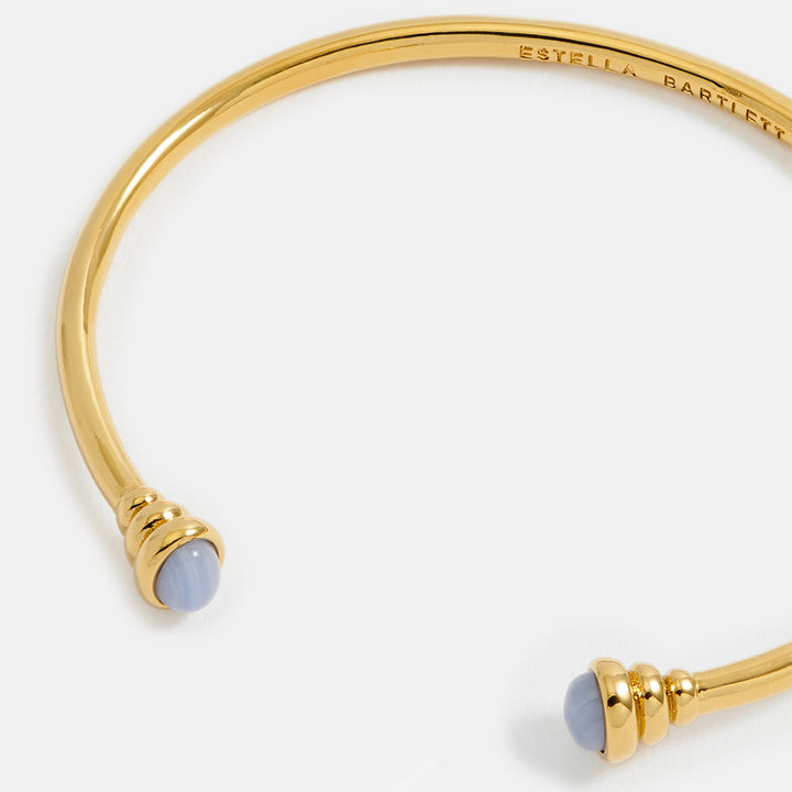 gold bangle bracelet with graduated ends with light blue gemstones
