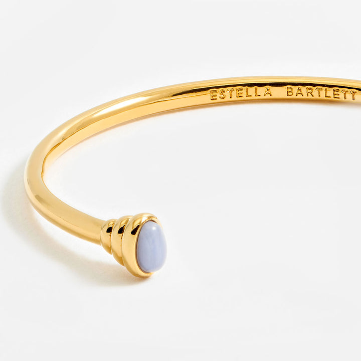 gold bangle bracelet with graduated ends with light blue gemstones