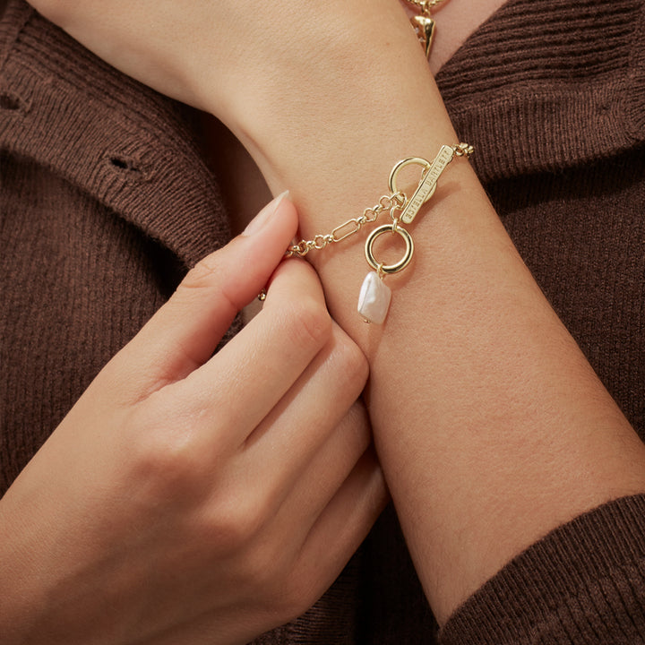 woman wearing gold bracelet with t-bar clasp and square pearl pendant