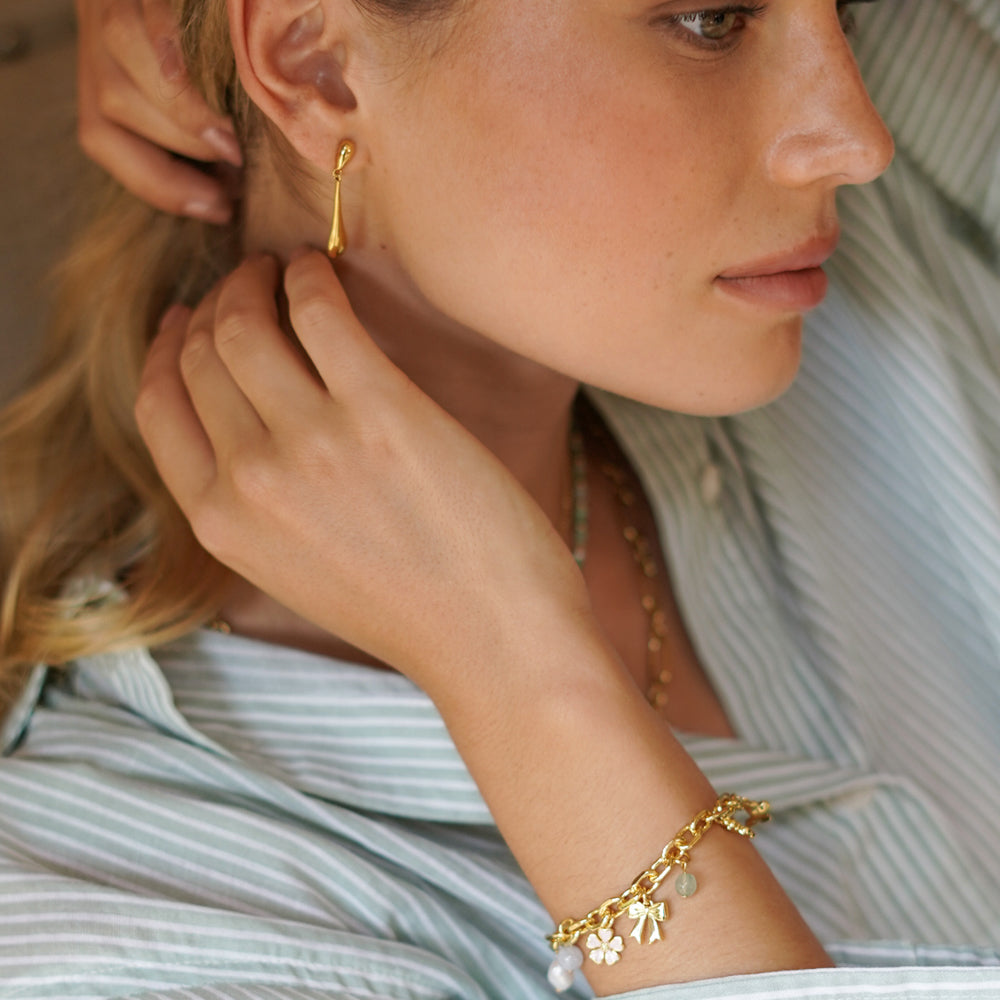 Woman wearing gold earrings and bracelet, close-up on face and arm.