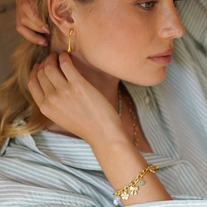 Woman wearing gold earrings and bracelet, close-up on face and arm.