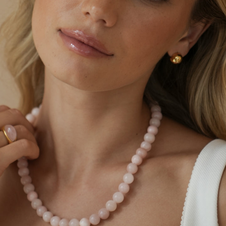 Close-up of a woman wearing a pink pearl necklace and gold earrings.