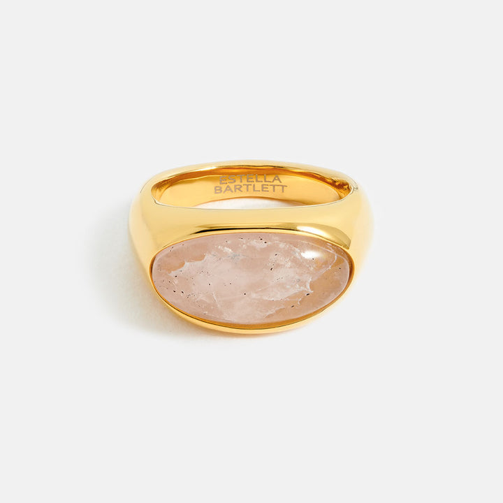 gold ring with pink oval gemstone on a light grey background