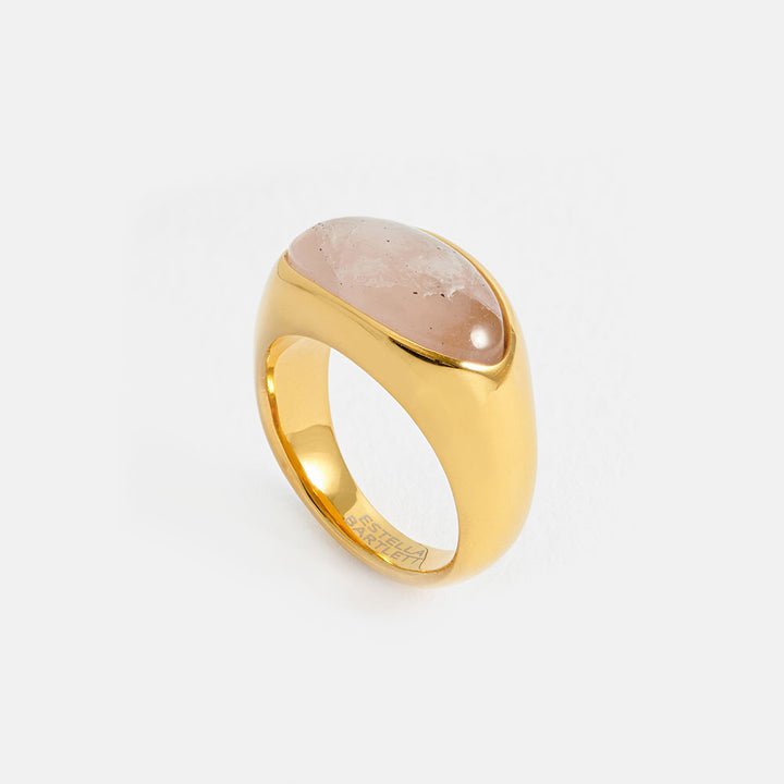 gold ring with pink oval gemstone on a light grey background