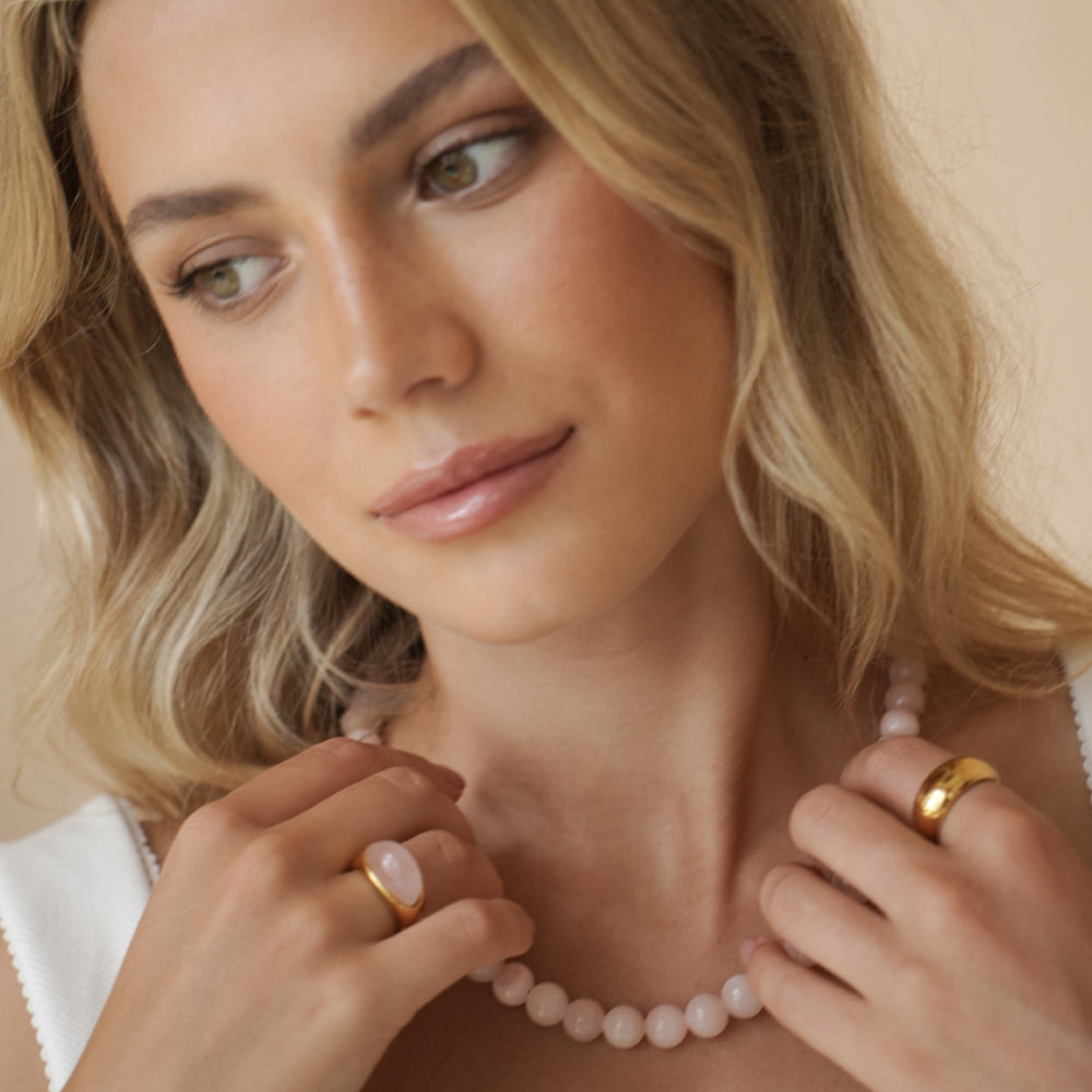 woman wearing pink beaded necklace, gold band ring, and pink gemstone & gold ring