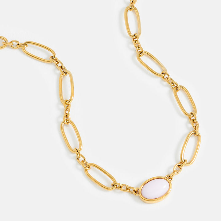 Gold chain necklace with a pink oval gemstone on a light grey background