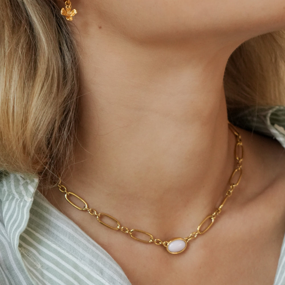 Gold chain necklace with a pendant on a person wearing a light green top.
