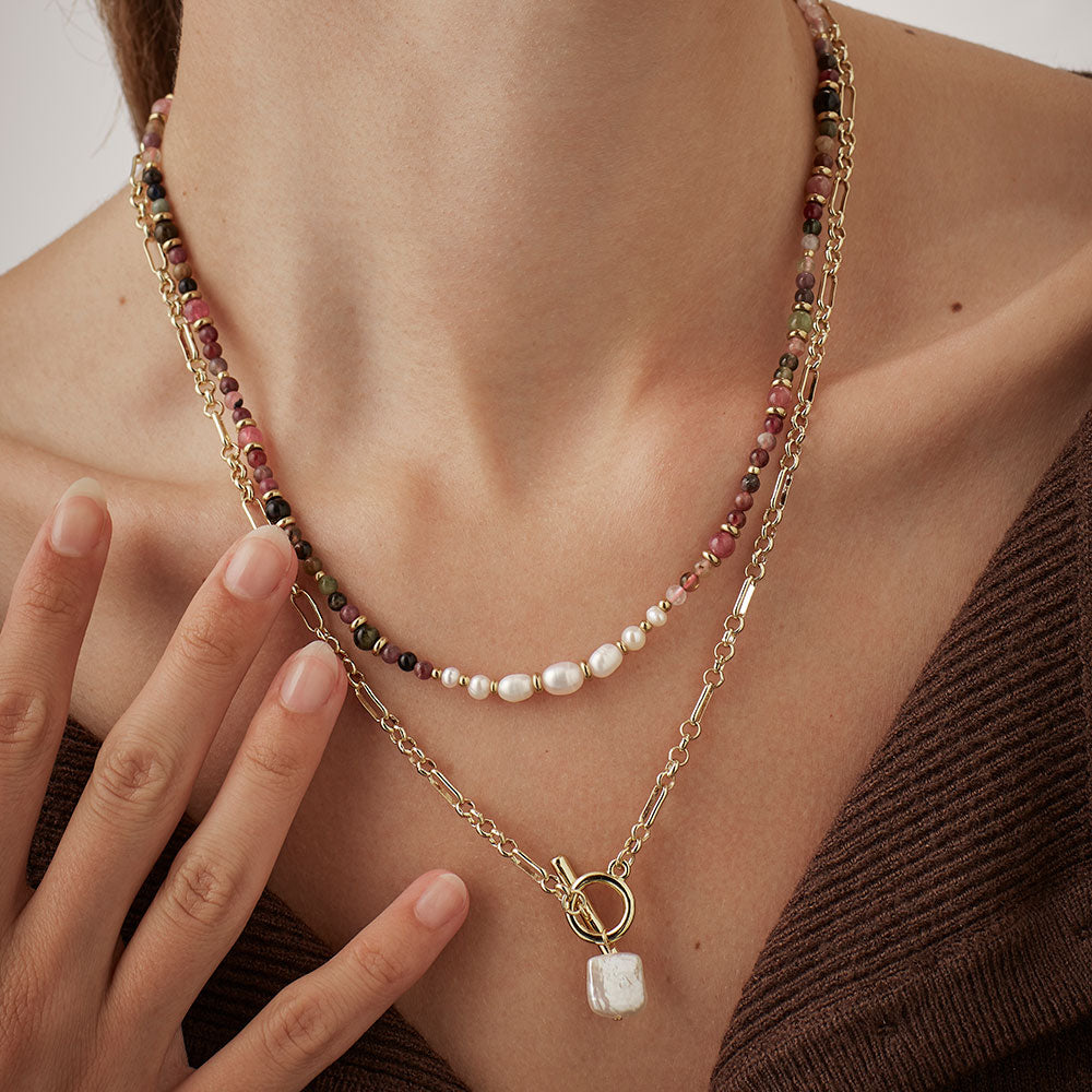 Close-up of a woman wearing a layered necklace with a hand touching her chest.