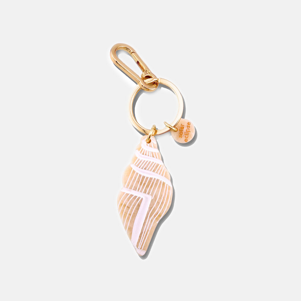 Gold bag charm with shell charm on a light grey background