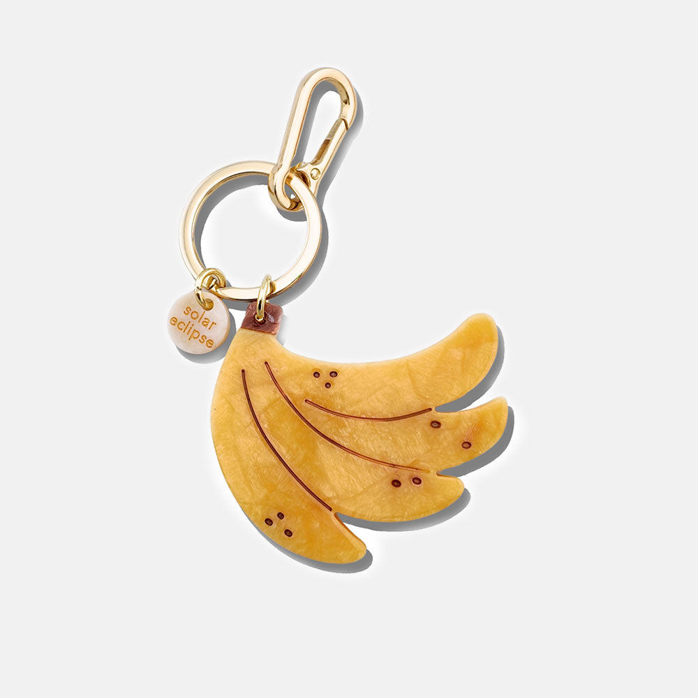 Banana-shaped bag charm with gold carabiner on a white background
