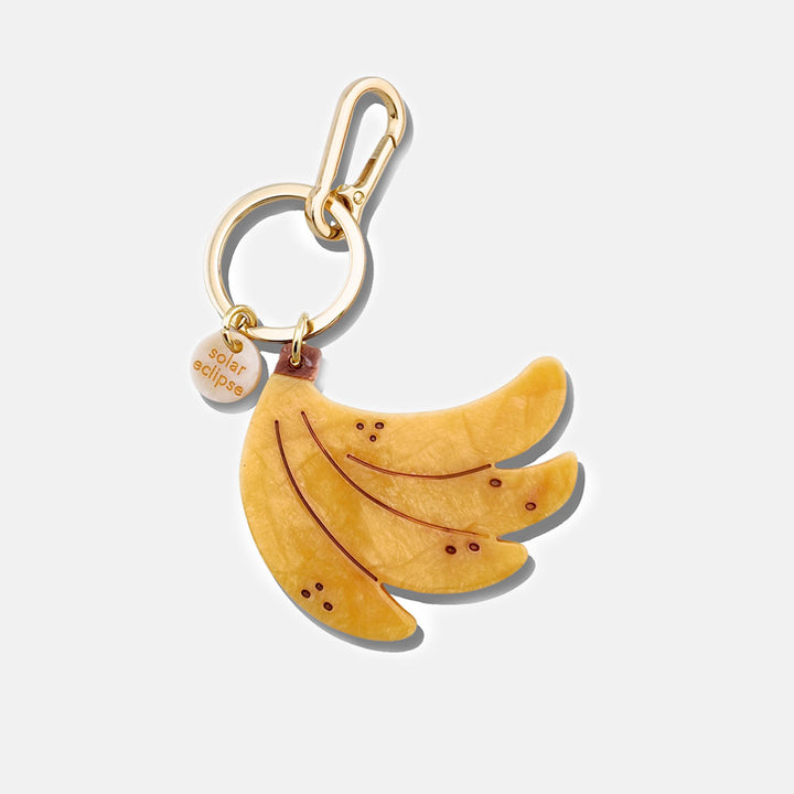 Banana-shaped bag charm with gold carabiner on a white background