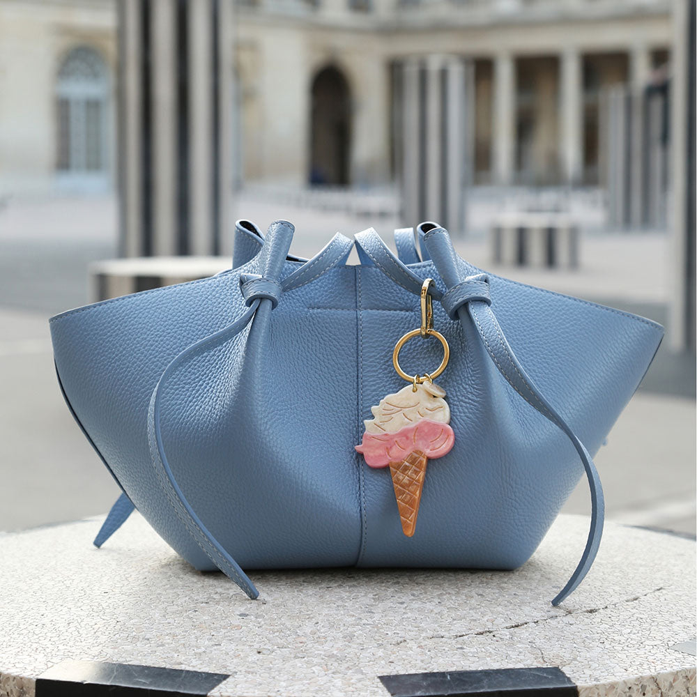 Blue handbag with an ice cream charm on a stone surface with a blurred architectural background