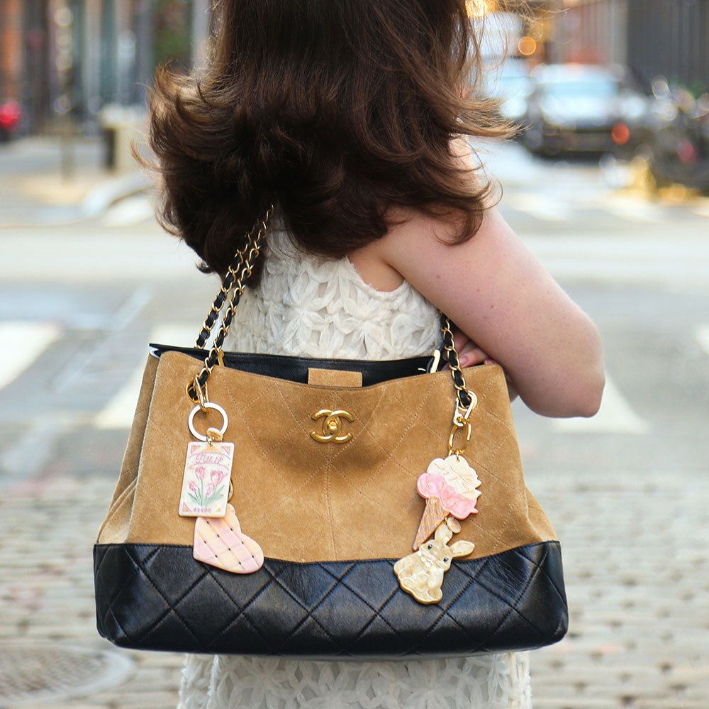 Person holding a tan and black handbag with decorative charms on a city street.