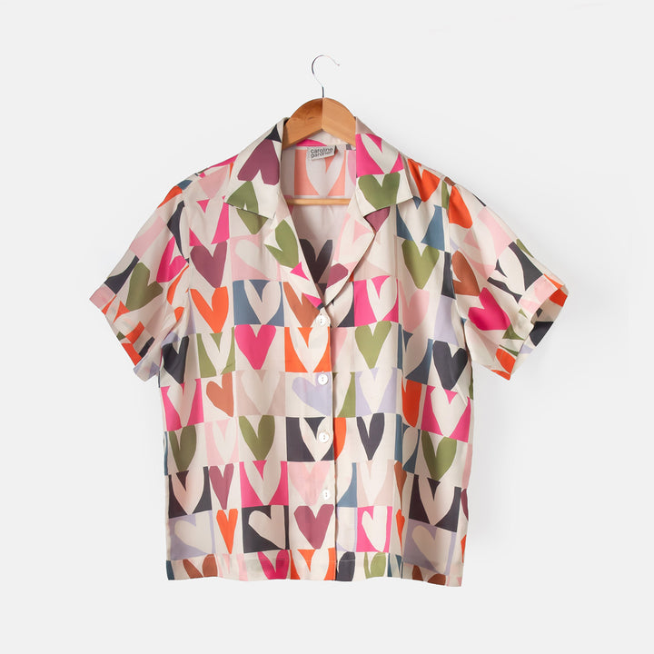 Colorful heart patterned shirt on a hanger against a white background