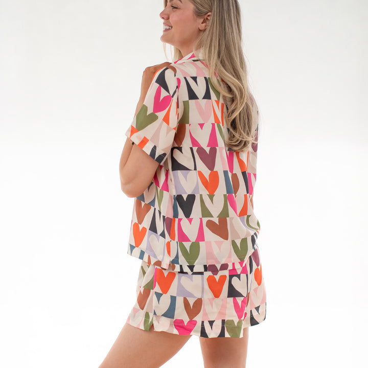 Woman wearing a colorful heart patterned short pyjama set on a white background