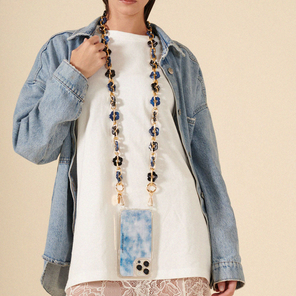 Person wearing a long phone chain with a blue and white patterned pouch, against a beige background
