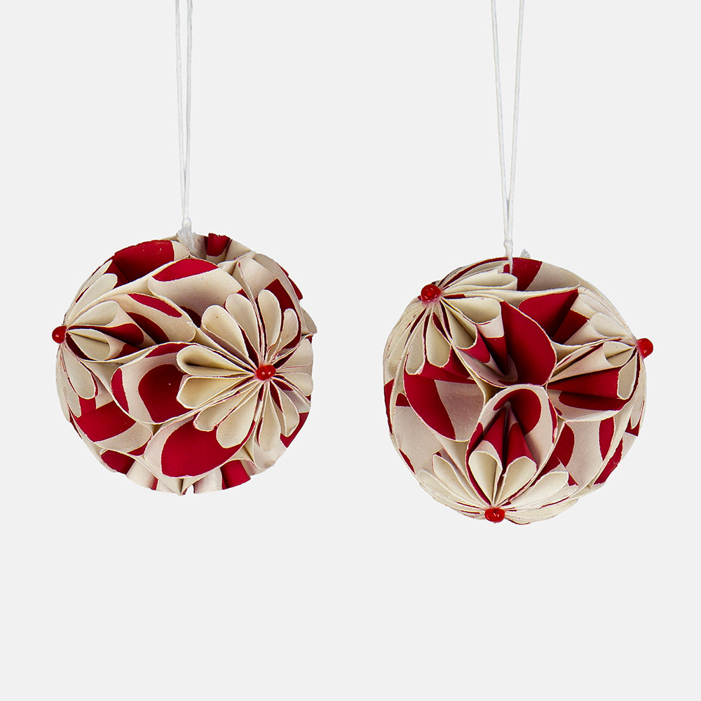 2 red and white paper christmas tree decorations with an intricate flower ball design, on a hanging string against a white background