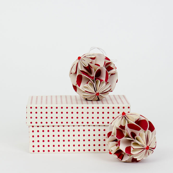 2 red and white paper christmas tree decorations with an intricate flower ball design and a white presentation box with red dots