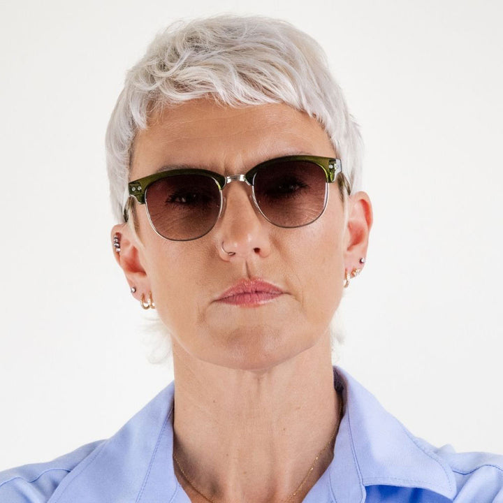 woman wearing green framed sunglasses with brown gradient lenses on a white background