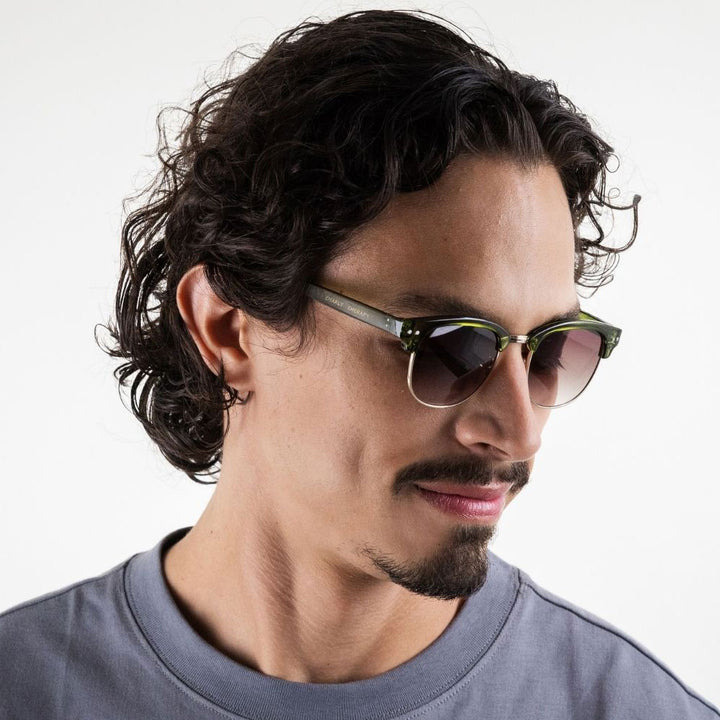 man wearing green framed sunglasses with brown gradient lenses on a white background