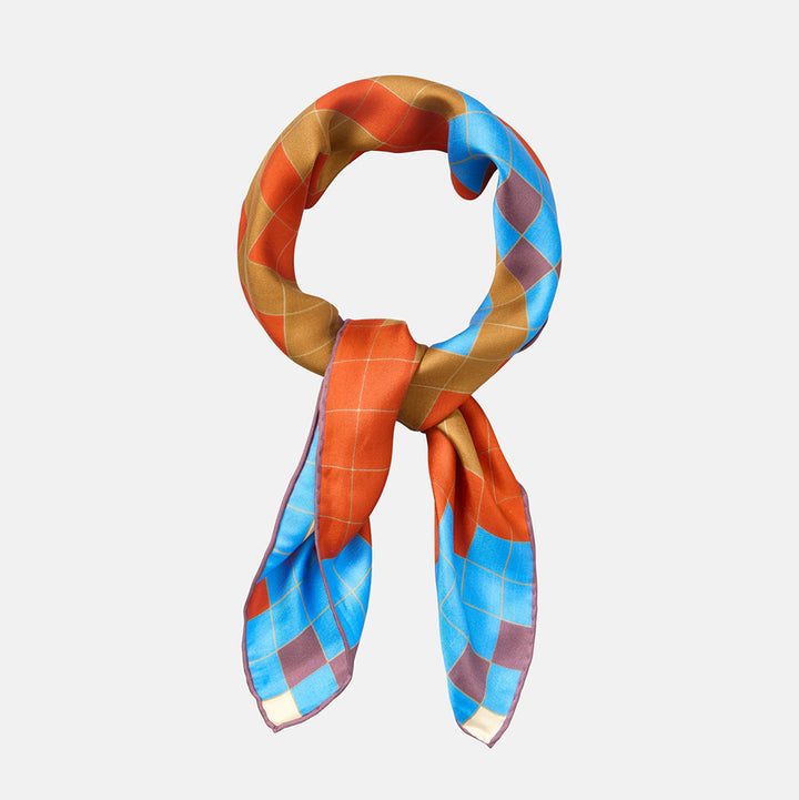 A silk scarf with a colorful argyle pattern in orange, gold, blue, and purple, styled in a loop on a light gray background.