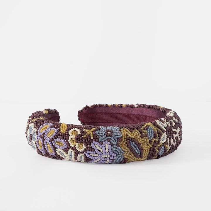 A wide, padded headband featuring a multicolor beaded floral pattern over a deep burgundy base, shown against a plain white background.