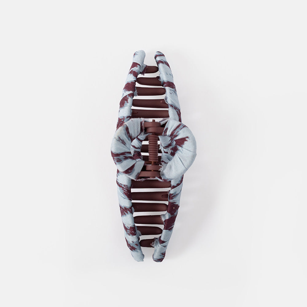 A spiral hair claw clip with a blue and Burgundy marble pattern, shown on a plain grey background.