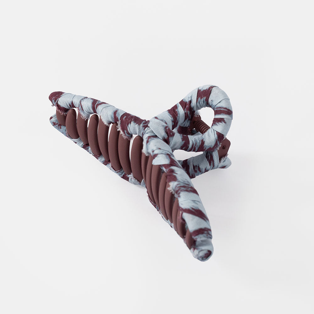 A spiral hair claw clip with a blue and Burgundy marble pattern, shown on a plain grey background.
