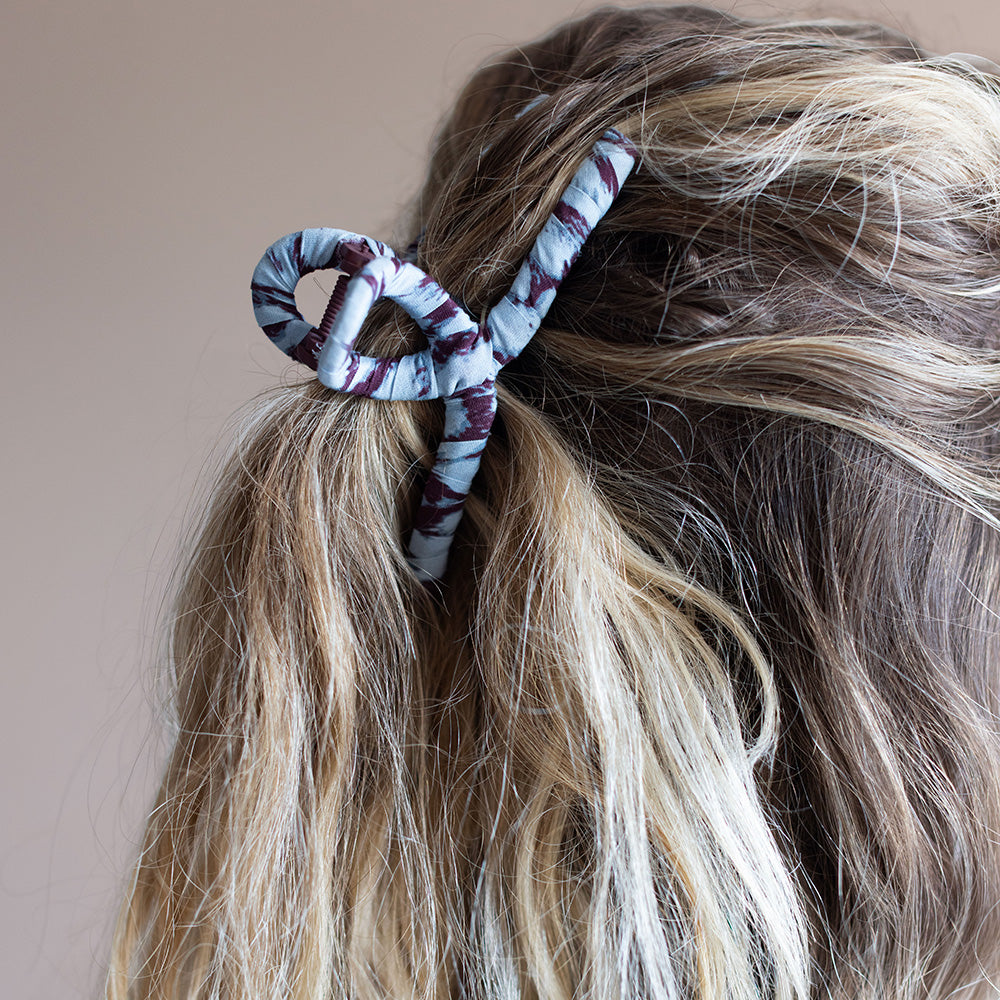 A spiral hair claw clip with a blue and Burgundy marble pattern, shown on hair.