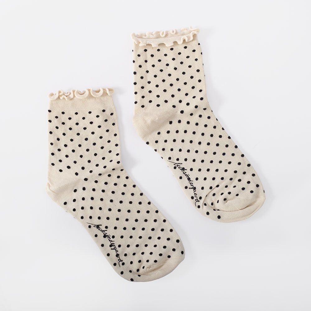 A pair of off white short socks with black polka dots and a frilled cuff, on a light grey background.
