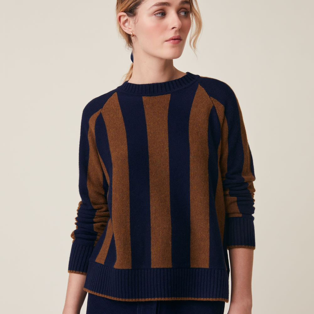 A woman wearing a navy and brown vertically striped knit sweater, photographed against a plain light beige studio background.