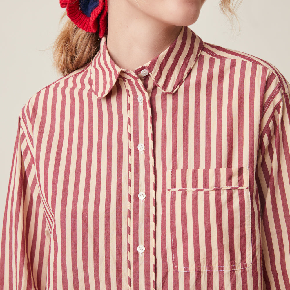 A close-up of a person wearing a long-sleeve button-up shirt with vertical red and cream stripes, featuring a classic collar and a chest pocket.