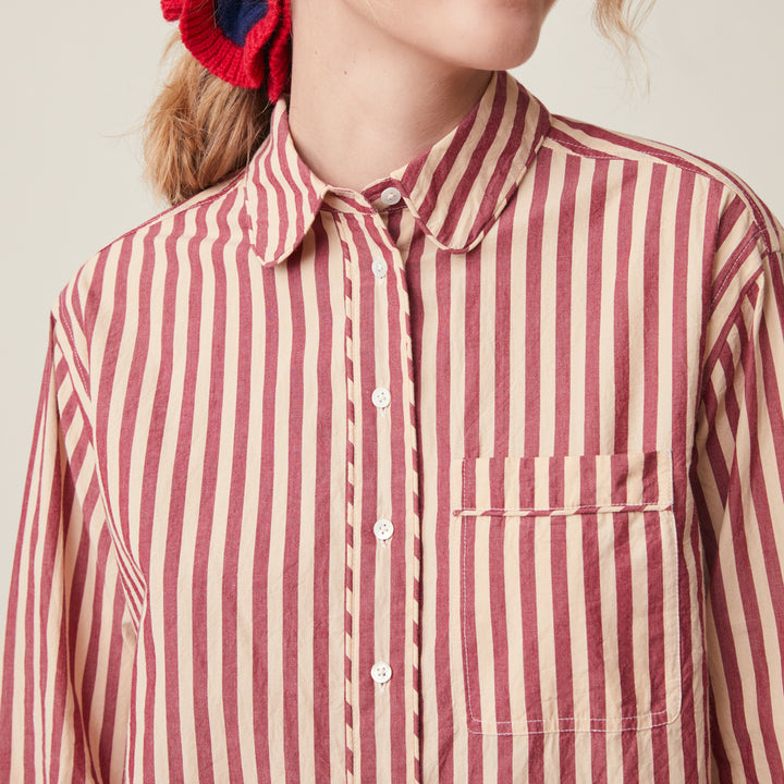 A close-up of a person wearing a long-sleeve button-up shirt with vertical red and cream stripes, featuring a classic collar and a chest pocket.