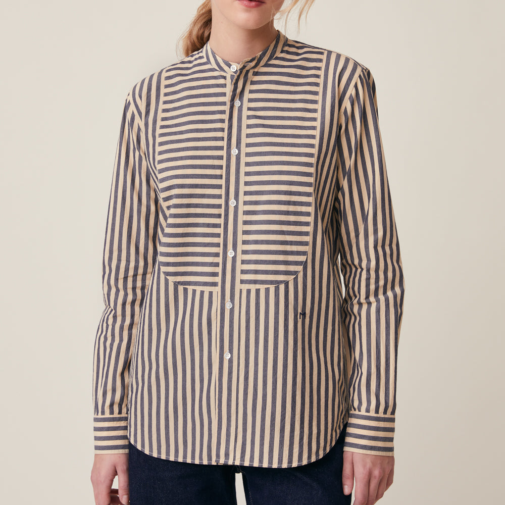 A woman wearing a long-sleeve button-front shirt with vertical navy and beige stripes, shown from the neck down against a plain light beige studio background.