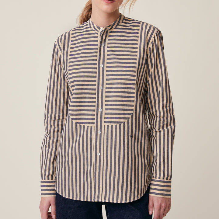A woman wearing a long-sleeve button-front shirt with vertical navy and beige stripes, shown from the neck down against a plain light beige studio background.