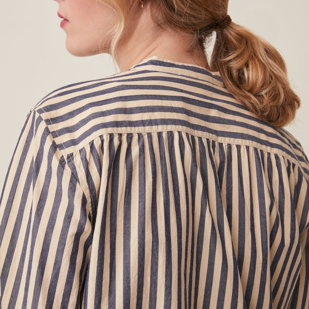 Close-up back view of a woman wearing a cream and navy blue vertically striped blouse with a gathered neckline.