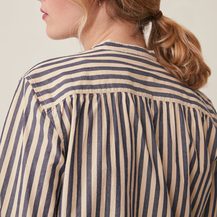 Close-up back view of a woman wearing a cream and navy blue vertically striped blouse with a gathered neckline.