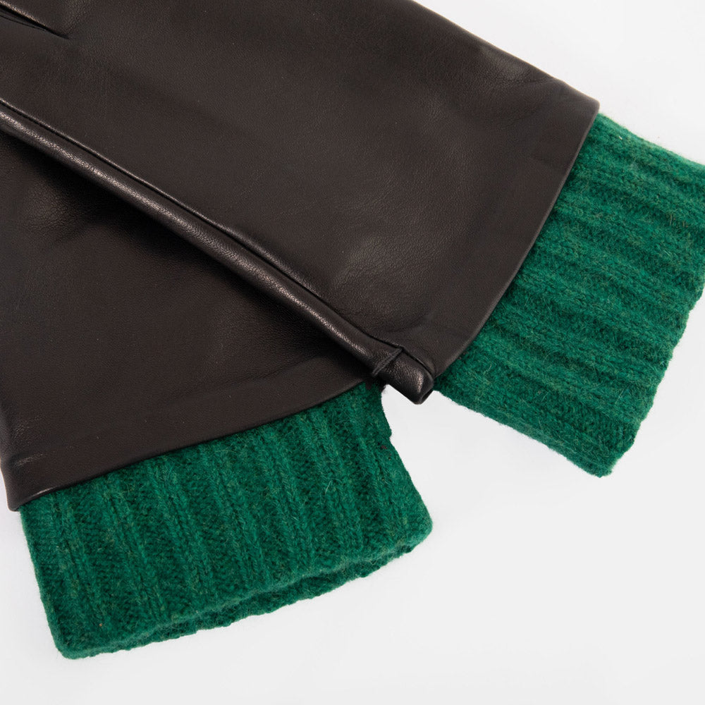 Close-up of a pair of black leather gloves with a contrasting green ribbed knit cuff, displayed flat against a light gray background.