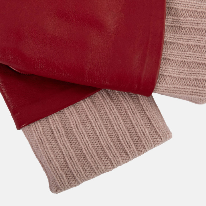 A close-up of a pair of red leather gloves with ribbed knit cuffs in a dusty pink colour, displayed flat against a light grey background.