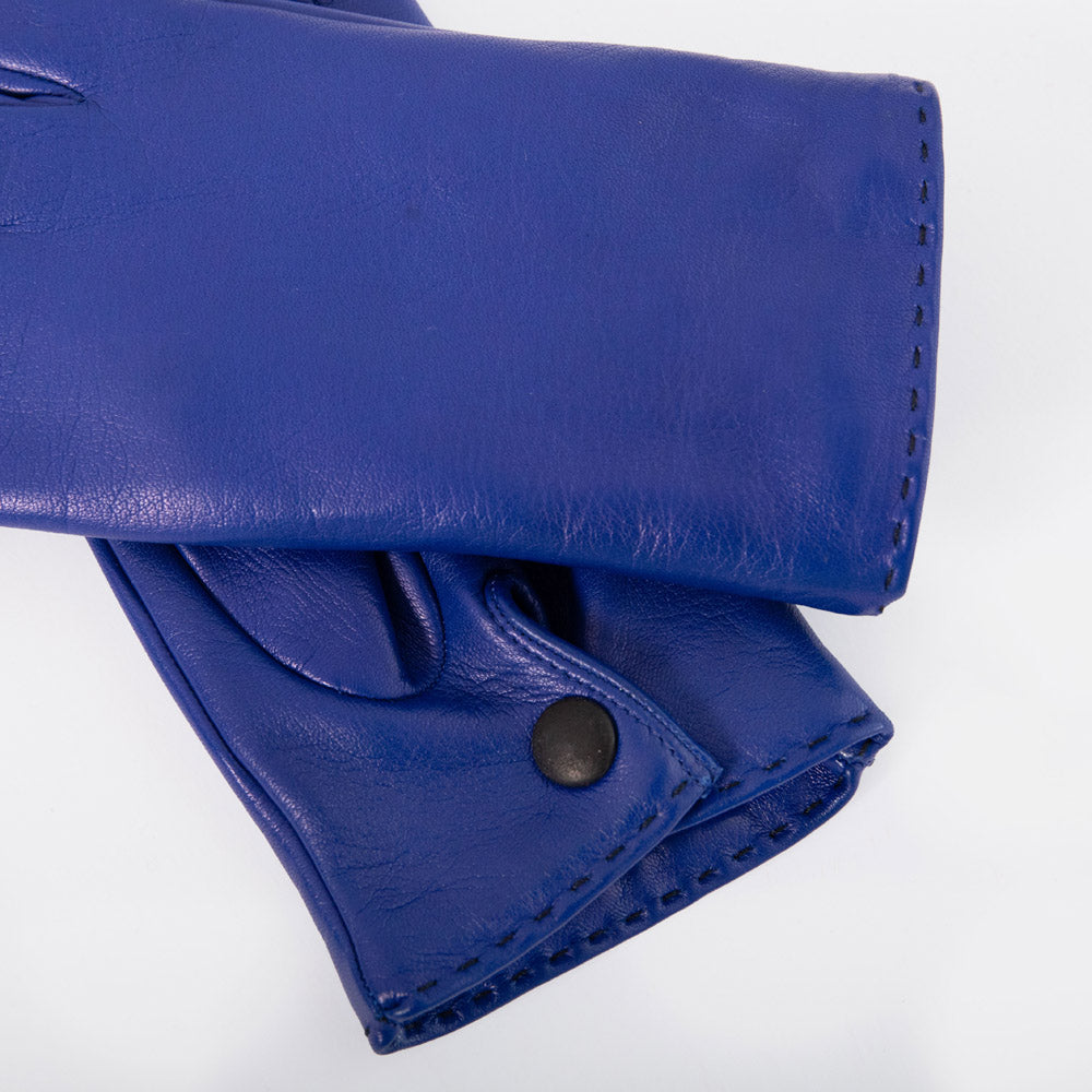 A close-up of a royal blue leather glove or mitten folded over on a white background, showing the smooth texture, stitching, and a dark snap button.