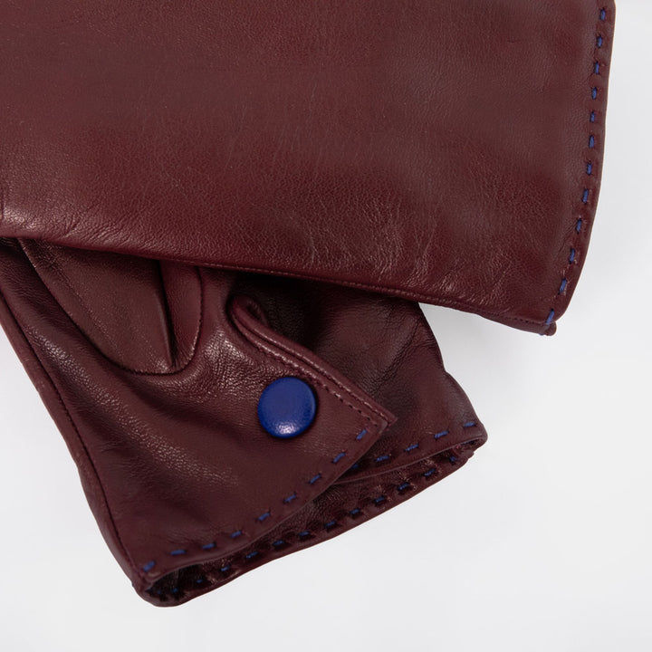 Close-up of a dark burgundy leather garment, showing the texture of the leather, blue contrast stitching, and a blue snap button closure on a white background.