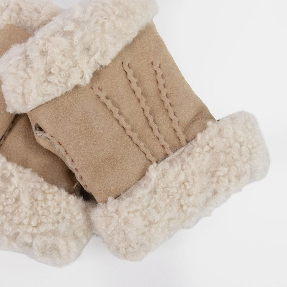 Close-up of a pair of beige suede wrist warmers with thick cream fleece cuffs and a decorative whipstitch pattern on the sides, set against a plain white background.