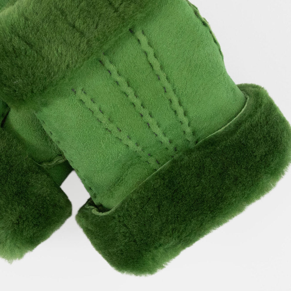 close up of a pair of women's green shearling wrist warmers with suede outer and fluffy wool cuff on a light grey background