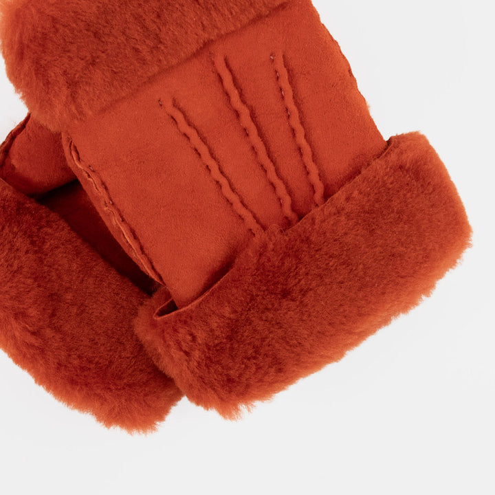 Close-up of a pair of rust-orange shearling-lined wrist warmers shown flat against a clean white background.