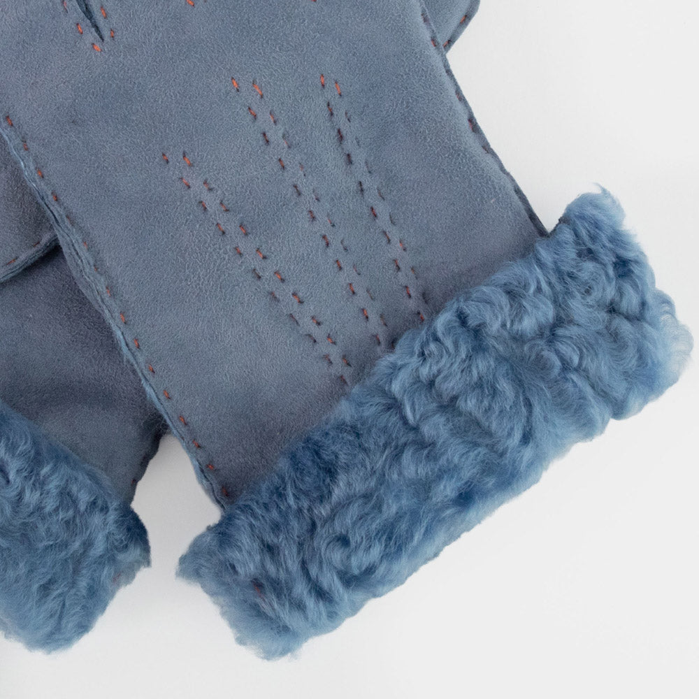 Close-up of a blue suede mitten with a thick, curly blue faux-fur cuff and subtle red-orange contrast stitching.