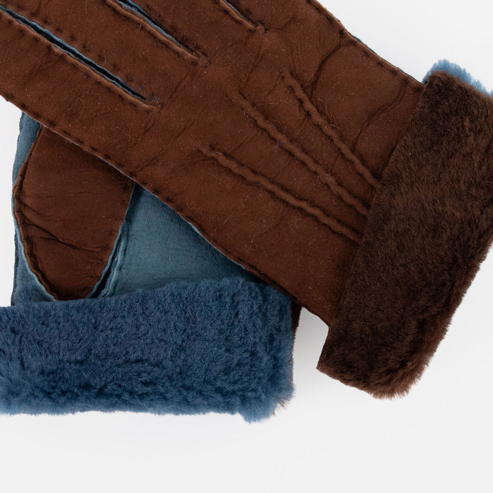 A close-up of a pair of brown leather gloves with dark brown faux fur trim and blue faux fur lining, shown on a plain white background.