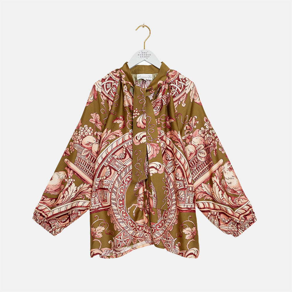A long-sleeve silk blouse with a brown base and a pink and beige baroque-style pattern, hanging on a white hanger against a light gray background.