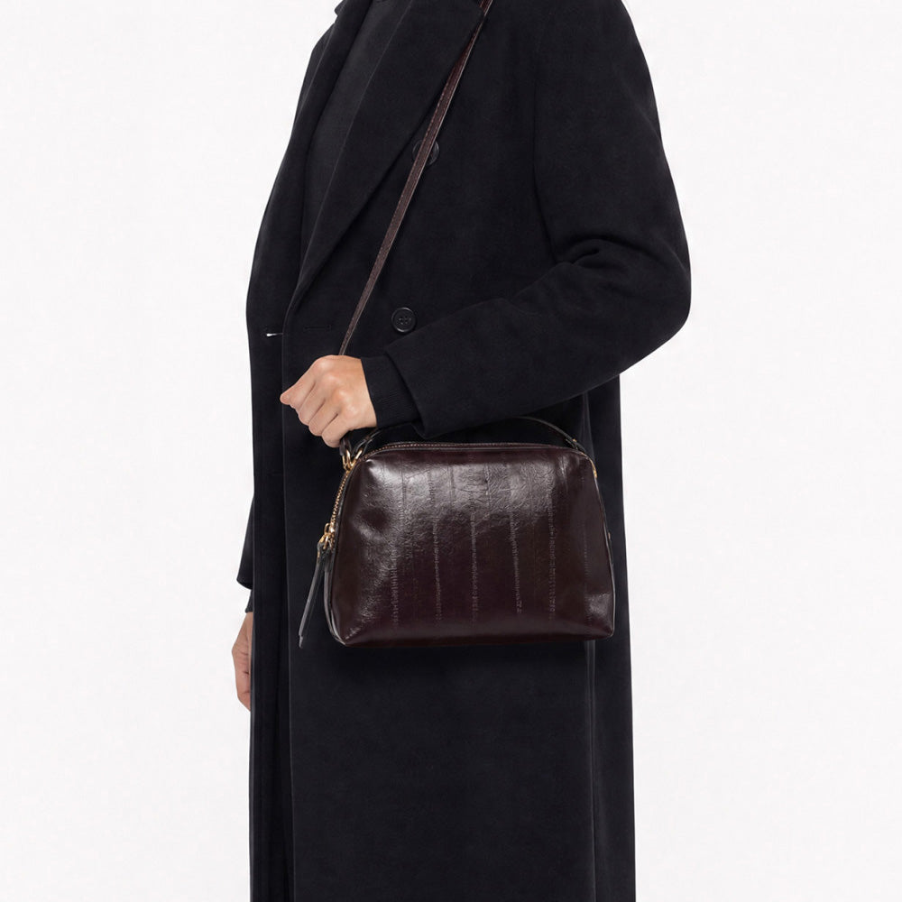 Woman in a long black coat wearing a dark burgundy leather bag across the body